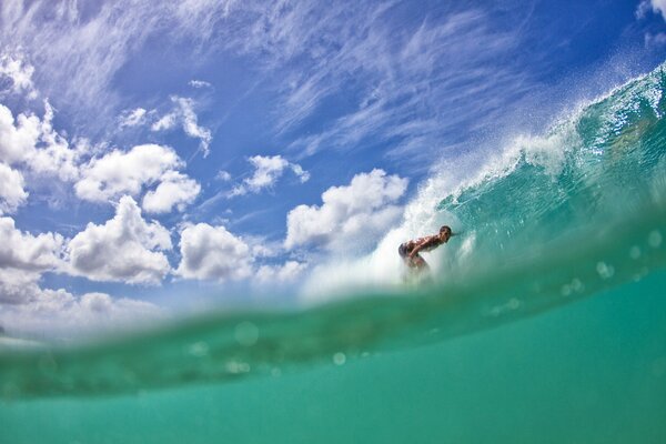Surfista en una ola verde bajo un cielo azul