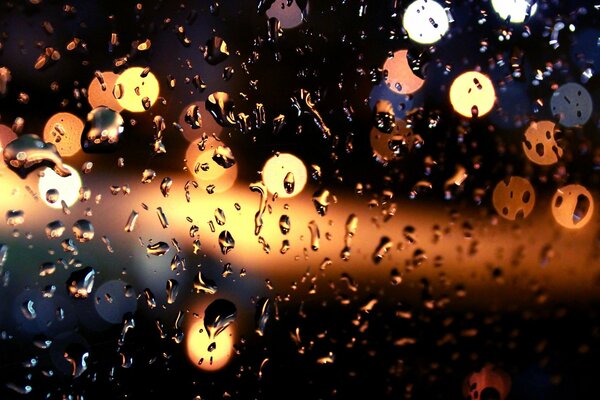 Lampki nocne prześwitujące przez szkło w kroplach deszczu