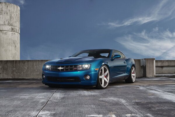 A blue chevrolet camaro stands in the parking lot against a beautiful sky