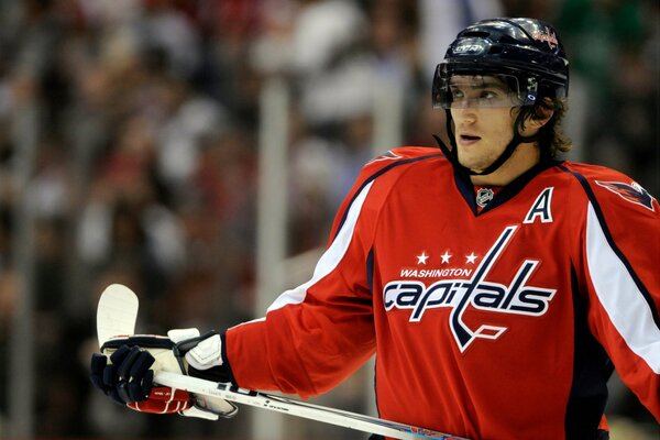 A hockey player in a red uniform holds a white stick in his hands