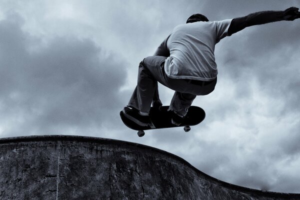 Uno skateboarder esegue un trucco su uno sfondo di nuvole grigie