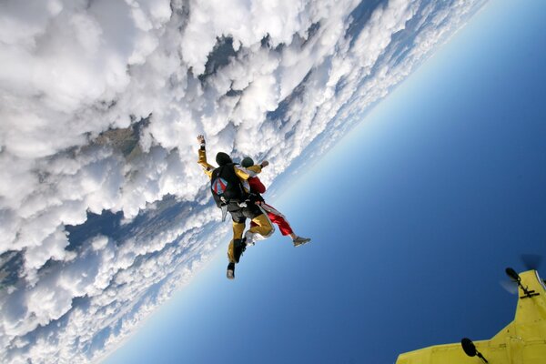 Dos skydivers hacen un salto en paracaídas contra las nubes y el cielo azul