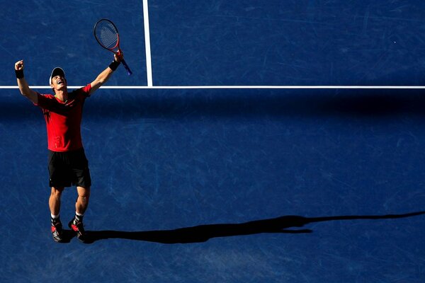 Le joueur de tennis en maillot rouge se réjouit de la victoire sur le court en soulevant la raquette