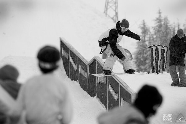 The snowboarder rolls on a board on a narrow fence in front of the audience