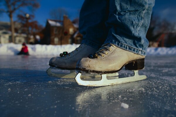 Homme en patins et en jeans sur la patinoire près de la maison. En arrière-plan, un homme dans une veste rouge est assis sur la glace