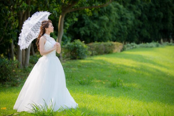 Asian girl in a wedding dress under a summer umbrella