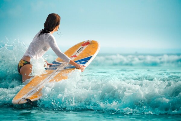 La imagen muestra las olas, el océano, una chica que sabe mucho sobre el deporte