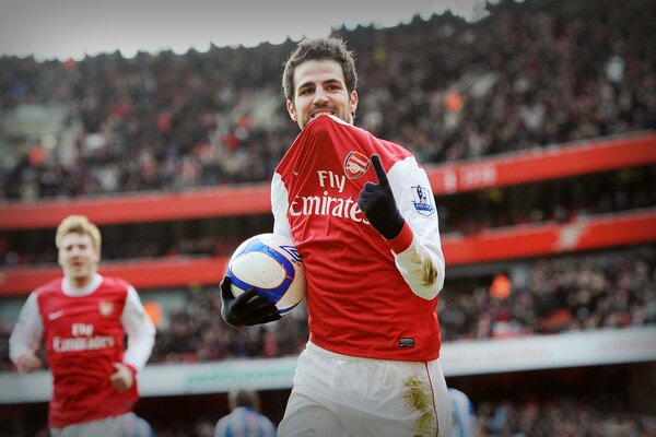 Joueur de football en uniforme rouge avec une balle dans la main grignote les dents d un t-shirt et montre le doigt vers le haut