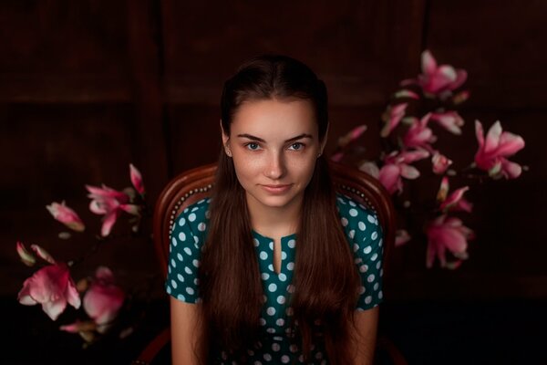 Una chica con un vestido de lunares se sienta en una silla contra un fondo de flores