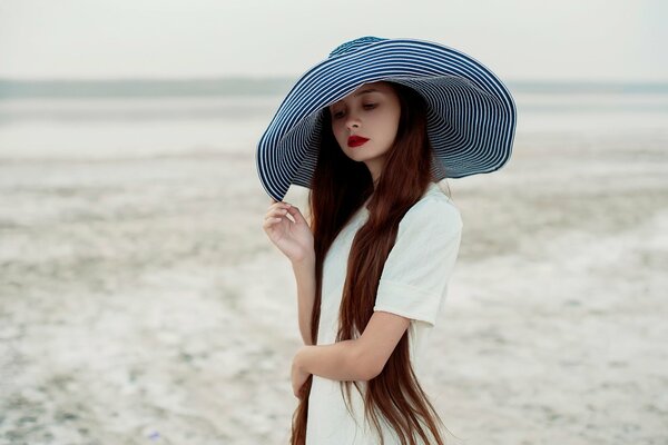 Una chica con un vestido blanco sostiene un sombrero de ala ancha a rayas