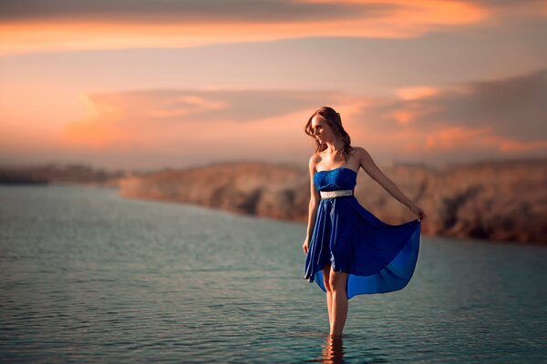 A girl in a blue dress is standing in the water