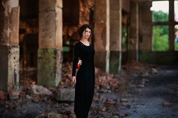 Una chica con un vestido negro con el pelo marrón con una pesa rusa en sus manos en el fondo de un edificio abandonado