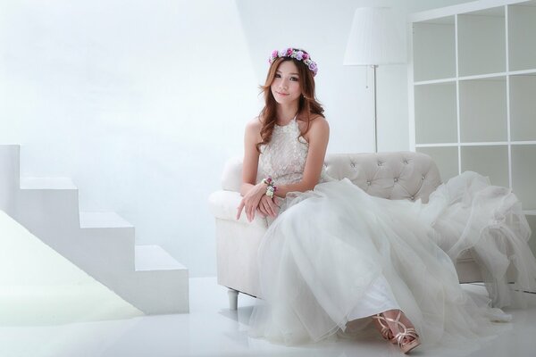 A girl with a wreath in her hair in a snow-white dress on a white sofa