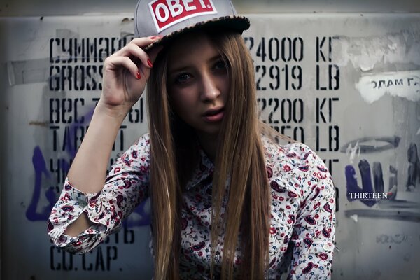 A young girl in a cap on the background of a wall with graffiti