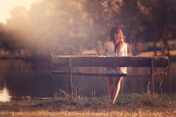 Девушка сидит на лавочке на берегу речки