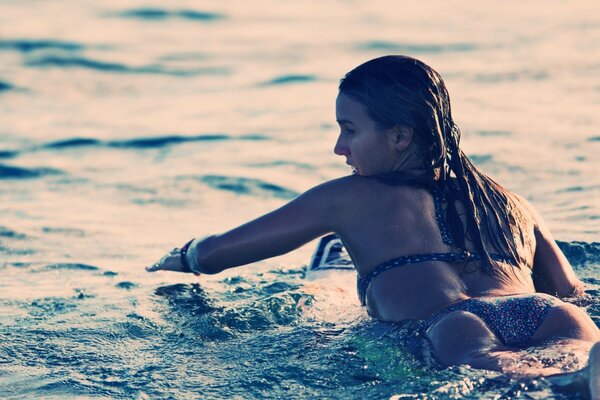 Fille en bikini nage sur une planche de surf