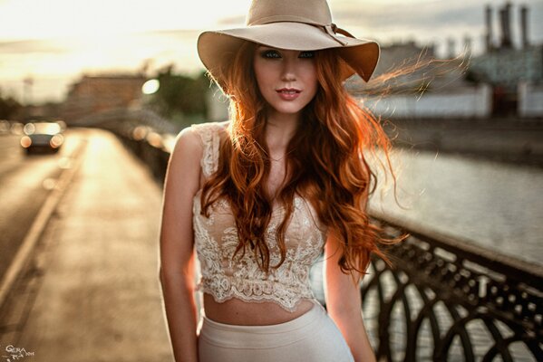 A red-haired beauty in a hat walks across the bridge