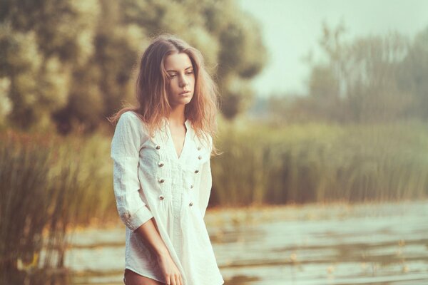 Sad girl in a white blouse on the background of a pond