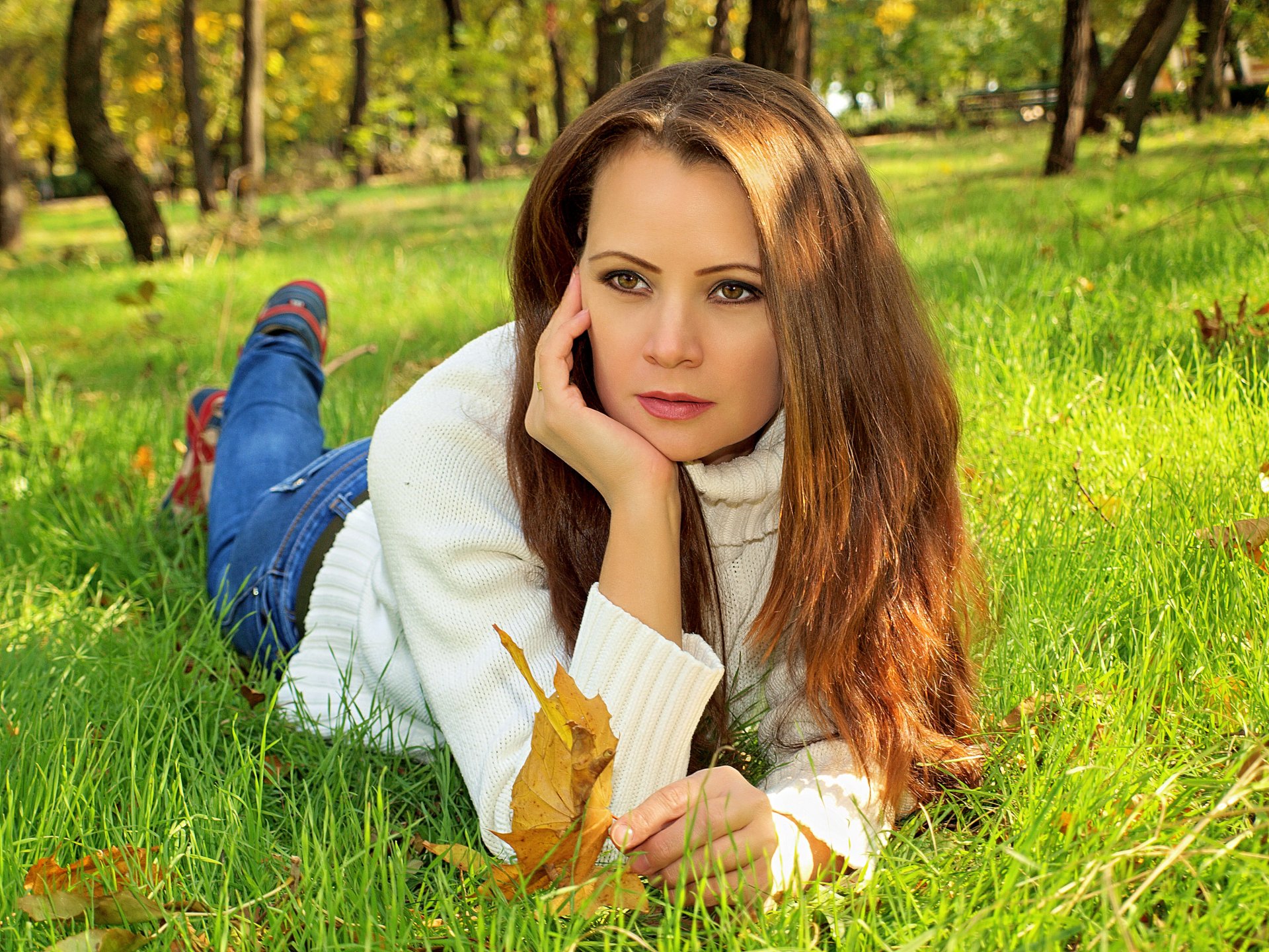 autumn park tree girl brown hair is on grass sweater jeans leaves yellow green blur