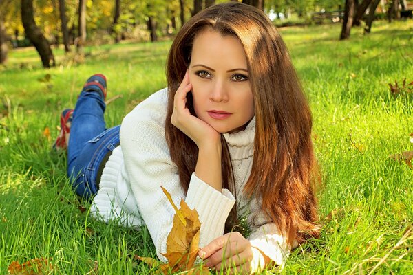 Красивая девушка с длинными волосами лежит на траве осенью