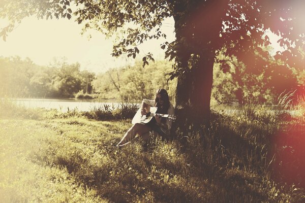 Mädchen am See unter einem Baum mit einer Gitarre in der Hand