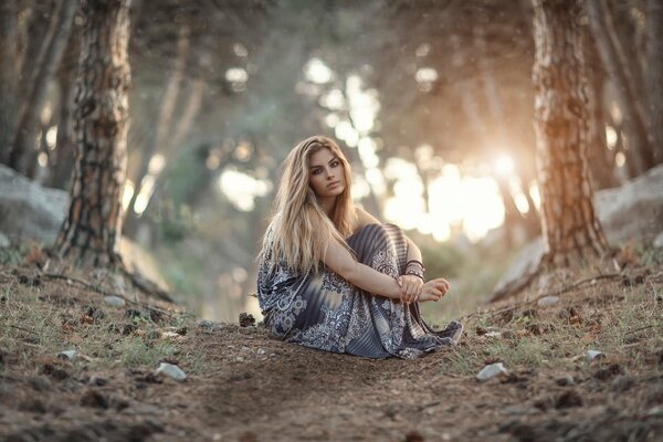 A girl is sitting in the forest against the background of sunset