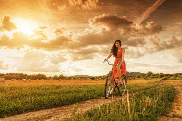 Chica monta una bicicleta en el camino al atardecer