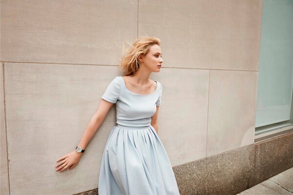 Modelo de chica en un vestido blanco posando contra una pared de fondo