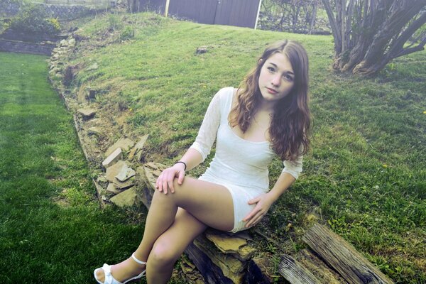 A girl in a short white dress is sitting on the ground