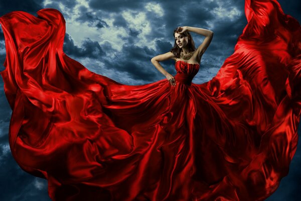 Una chica con un vestido largo rojo en el fondo de un cielo sombrío