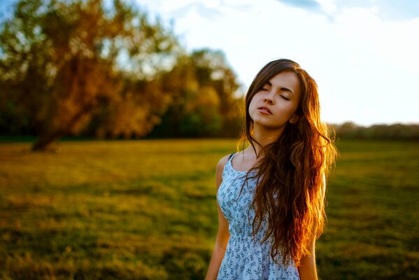 A girl with long hair and closed eyes is standing in a meadow