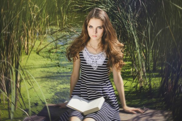 A brown-haired girl is sitting in the reeds with a book