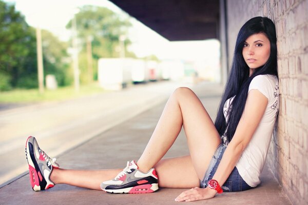 A girl in sneakers is sitting on the wall