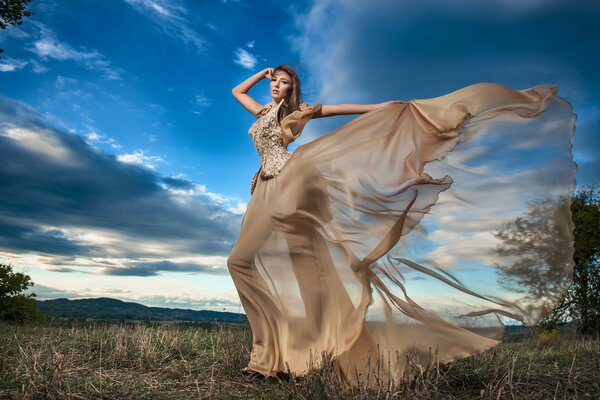 Ein Mädchen in einem schönen Kleid posiert auf einem Himmelshintergrund