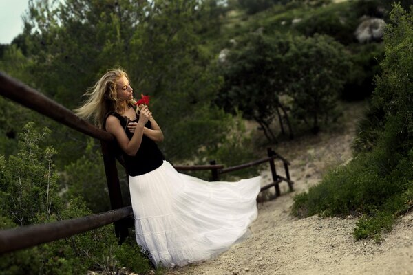 Ragazza in gonna aerea bianca con fiore rosso nelle mani