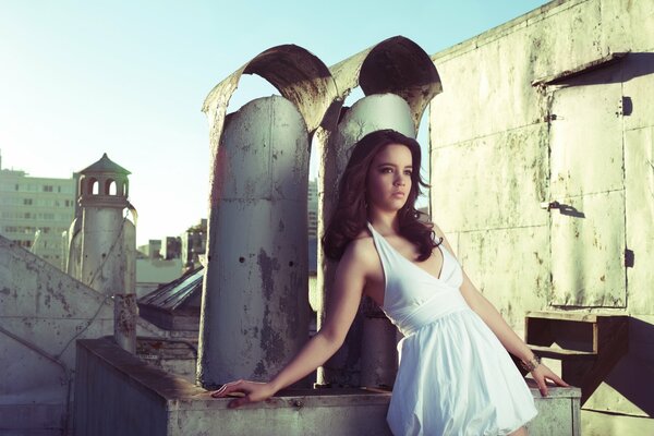 Una chica con un vestido blanco en el fondo de las tuberías y el techo de un edificio