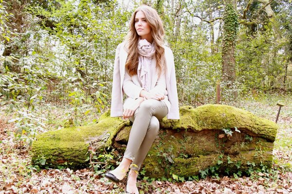 Model Clara Alonso in a scarf sits on a log