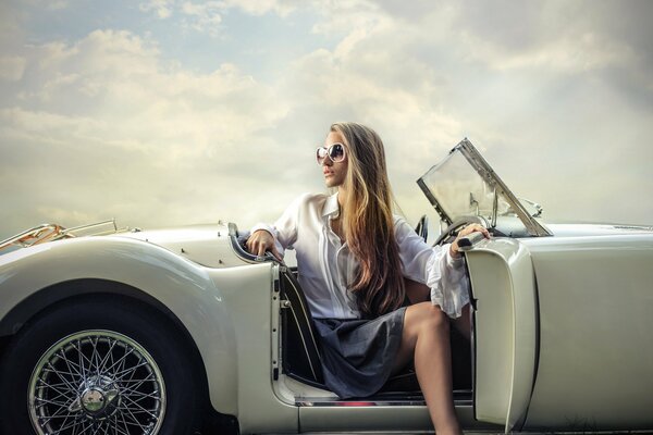 A girl with glasses poses against the background of a white car