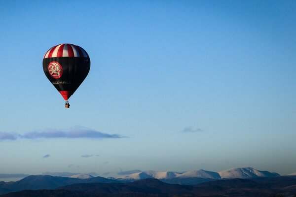 Ein dunkler Ballon fliegt durch den Himmel vor dem Hintergrund der Berge