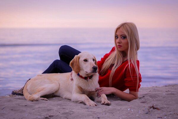 Jovencita rubia con perro en la orilla del mar