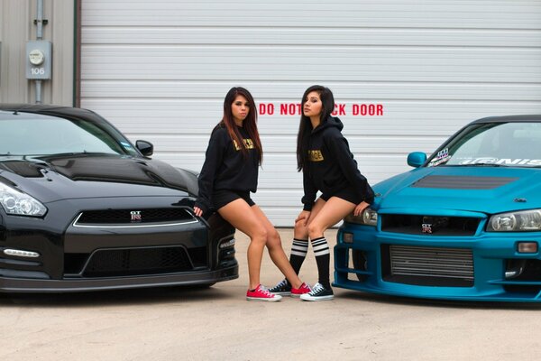 Two girls posing at cool cars