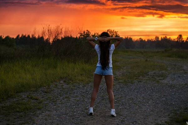 A sporty beautiful girl, against the background of a beautiful landscape-an eternal sunset and a life of approaching clouds and summer rain