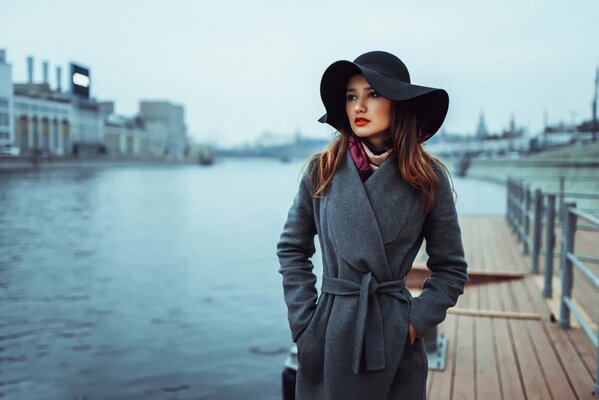 Ragazza con cappello nero e capelli castani sullo sfondo del molo