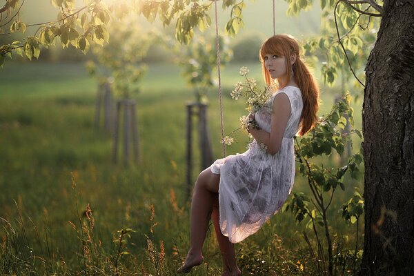 Ragazza con fiori su un altalena sotto un albero