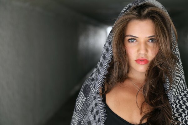 A girl wrapped in a checkered gray shawl walks through the tunnel