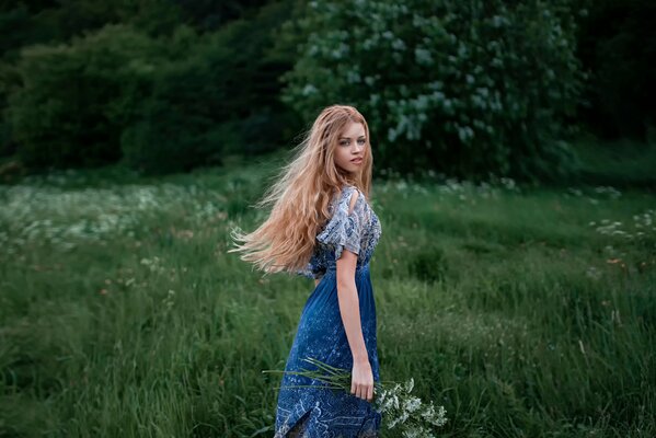 A lovely girl with a charming look and long hair in nature with a bouquet of flowers