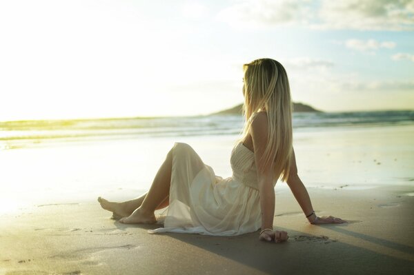 A girl in a sundress is sitting on the sand