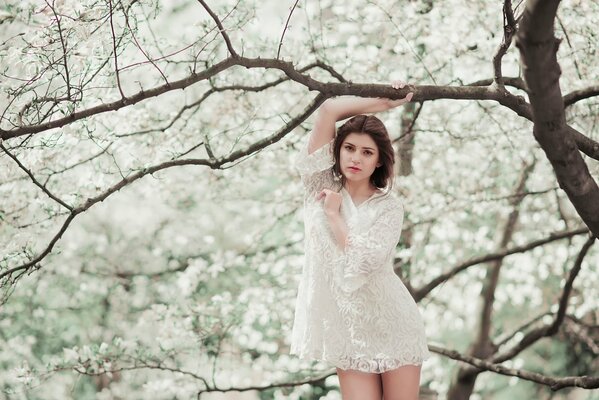 Chica en un vestido blanco ligero junto a un árbol en flor