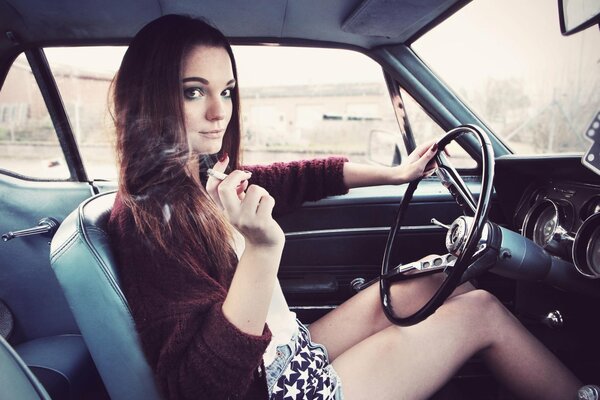 A girl holds a cigarette at the wheel of a car