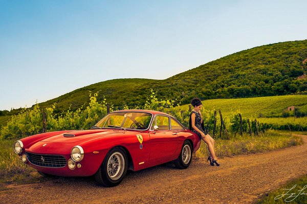 A beautiful girl is leaning on a red Ferrari in a field